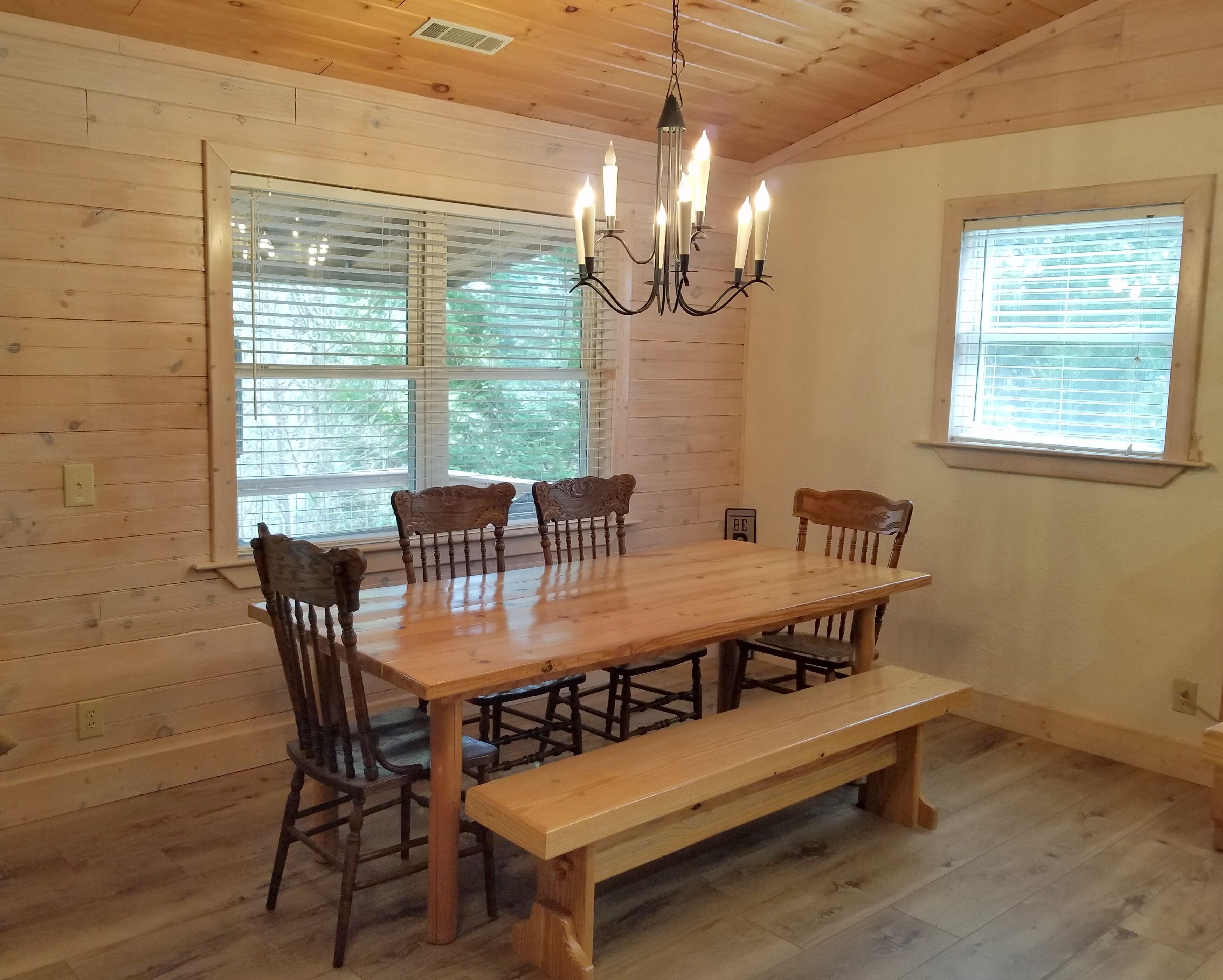 Une salle à manger en bois avec une grande table, quatre chaises, un banc et un lustre.