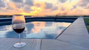 A glass of red wine on a poolside table with a sunset view.