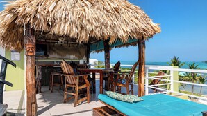 A wooden structure with a thatched roof, a bar area, and seating with a view of the ocean.