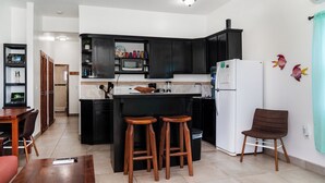 A modern kitchen with dark cabinets, a white refrigerator, and a dining area with wooden stools.
