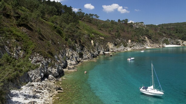 A coastal landscape with clear turquoise waters, rocky shoreline, and a sailboat. -  Sea view with terrace and garden for hiking, sailing, beach ... (Crozon)