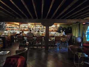 Um bar com vigas de madeira, poltronas de couro e diversas garrafas nas prateleiras.