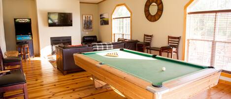 A pool table in a room with wooden floors, a television, and a fireplace.