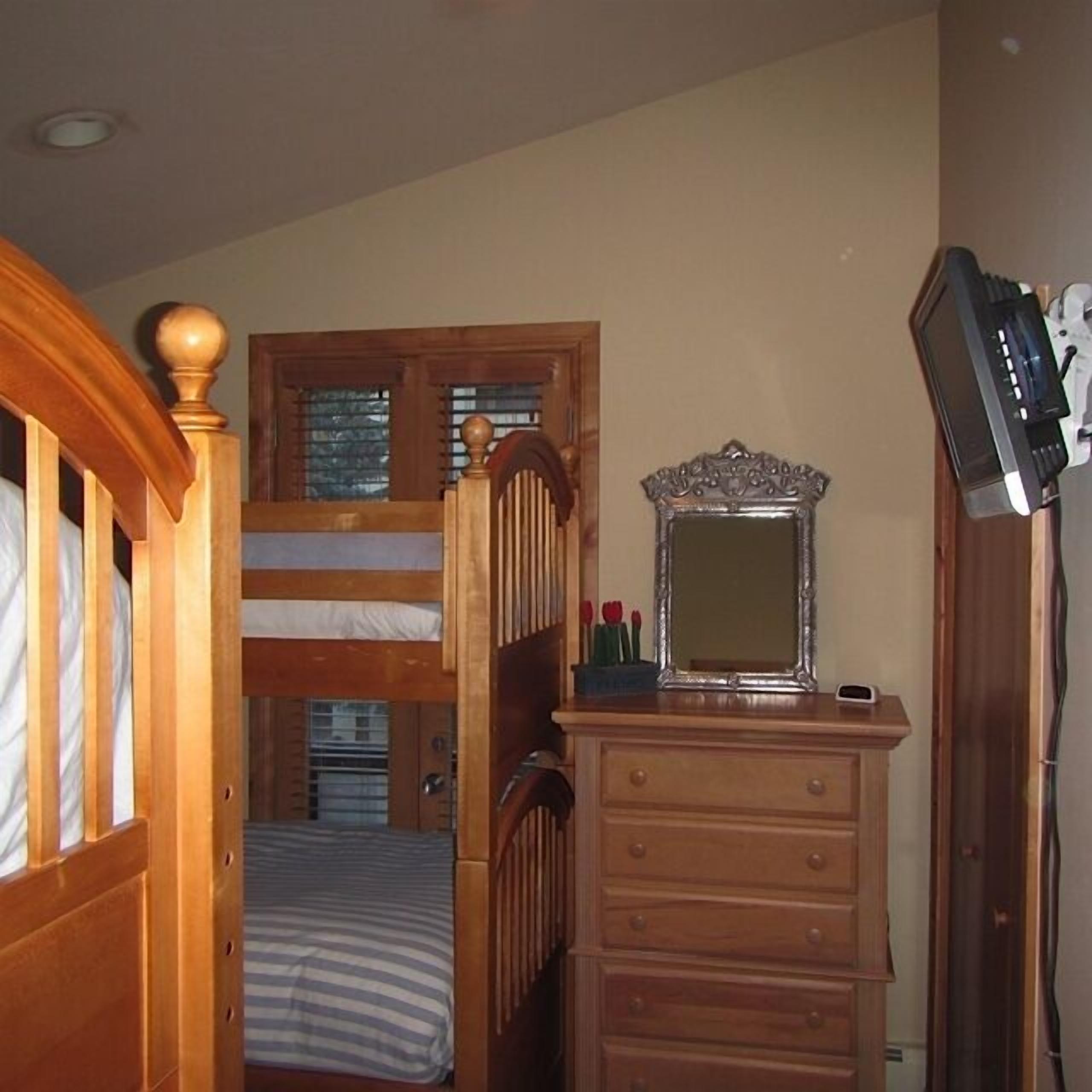 Une chambre avec un lit superposé, une commode avec un miroir et un téléviseur posé sur un meuble.