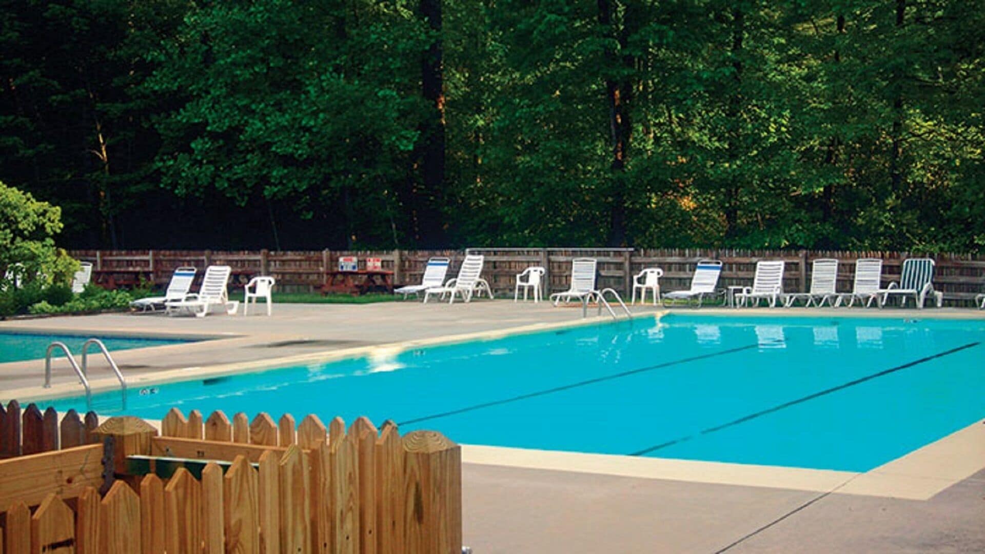 A swimming pool with lounge chairs and a wooden fence.