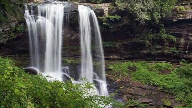 Ein Wasserfall stürzt über eine felsige Klippe, umgeben von üppigem Grün.