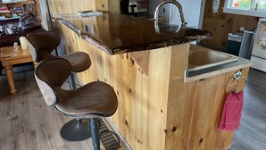 Una zona de bar con barra de madera, un lavamanos y taburetes.