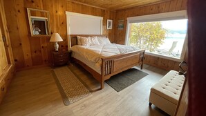 Un dormitorio con paneles de madera, una cama, mesita de noche, lámpara y ventana con vistas.