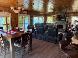 A wooden cabin interior with a dining area, seating, a fireplace, and a television.