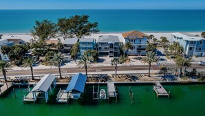 Un hotel frente al mar con varias construcciones, un puerto deportivo con barcos amarrados y una playa al fondo.