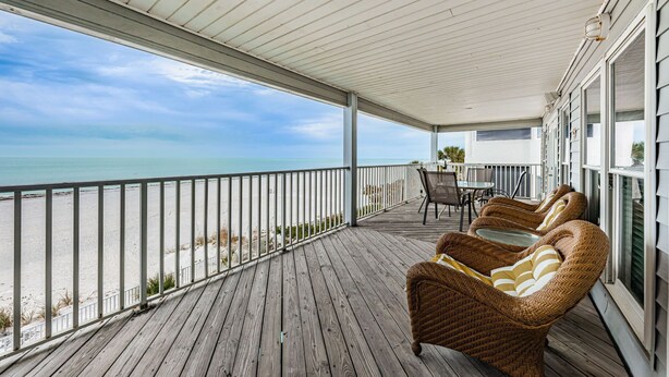 Una terraza de madera con mobiliario de mimbre y vista al mar.