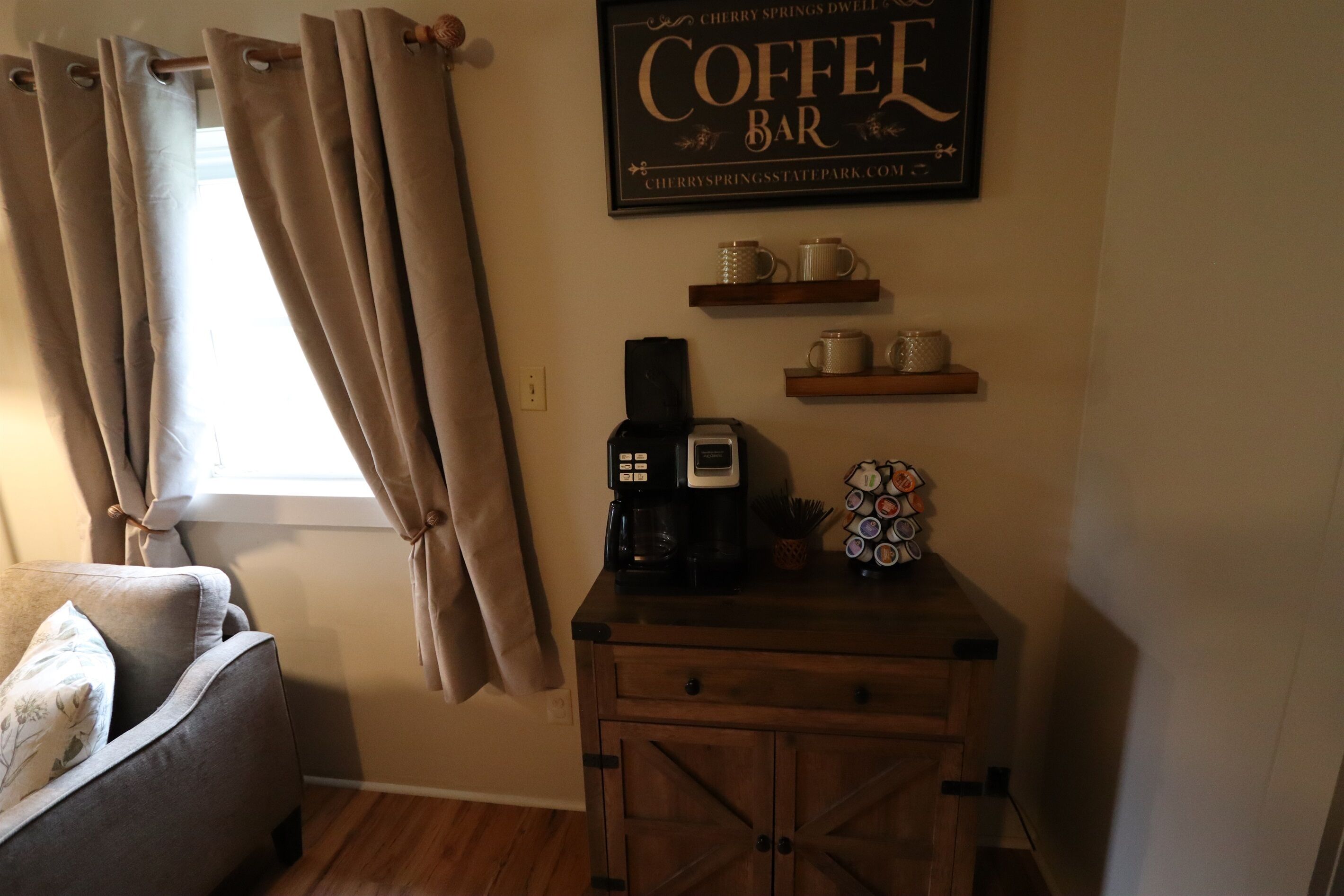 A cozy room with a coffee bar, a sofa, and a window with curtains.