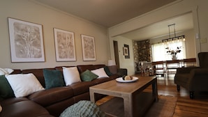 A living room with a brown leather sofa, a wooden coffee table, and framed botanical prints on the wall. - Hot Tub Stream Stargazing Field Game Rm Telescope (Coudersport)