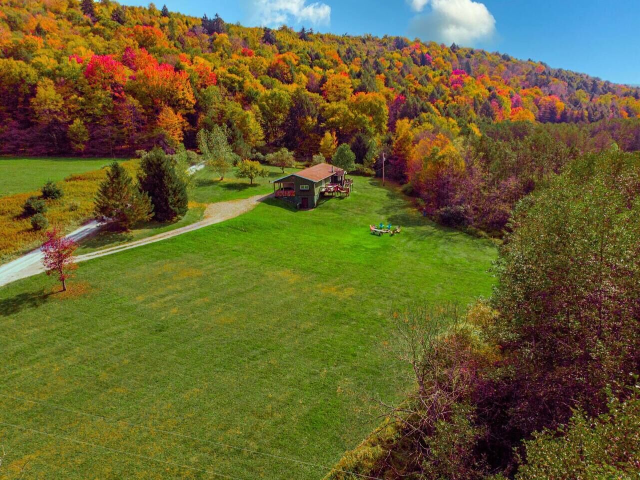 Une propriété rurale avec une petite maison entourée d’une pelouse bien entretenue et d’une colline boisée.