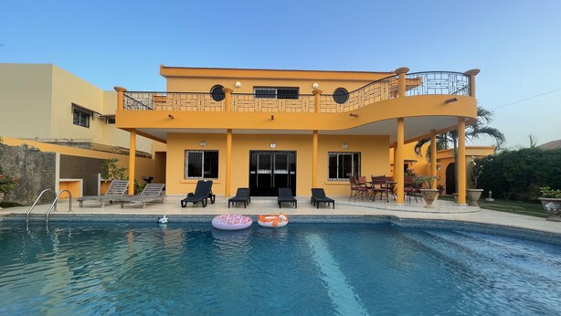 A two-story building with a swimming pool, lounge chairs, and a covered patio area.