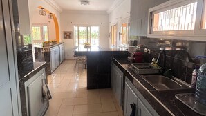 A modern kitchen with a central island, a dining area with a table and chairs, and a view of the outdoors through large windows.
