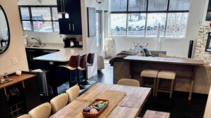 A modern kitchen with a wooden dining table, chairs, and a bench. There is a window with a view of the outside, a kitchen island, and a refrigerator. - Lofts 2-A-Stunning Condo Right Across From Ski Resort (Brian Head)
