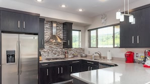 A modern kitchen with dark cabinetry, stainless steel appliances, a tiled backsplash, and a large island with a built-in sink. - Lofts 2-A-Stunning Condo Right Across From Ski Resort (Brian Head)
