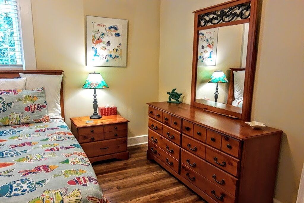 Une chambre à coucher comprenant un lit, une commode, une table de chevet, une lampe et un miroir.