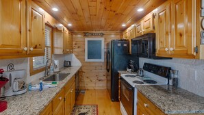 A compact kitchen with wooden cabinets, granite countertops, a refrigerator, stove, and a sink.