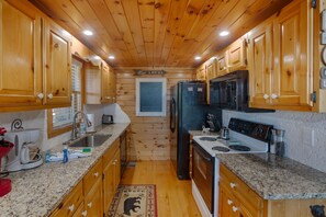 A compact kitchen with wooden cabinets, granite countertops, a refrigerator, stove, and a sink. - Amazing view! hot tub, sauna, game-room, pool, wood fireplace and firepit  (Sevierville)