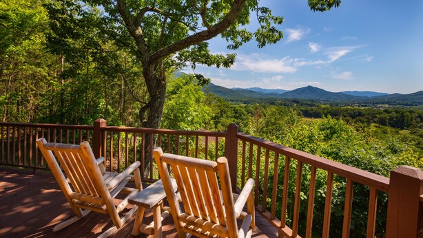 A wooden deck with two rocking chairs overlooking a forested landscape with mountains in the distance.