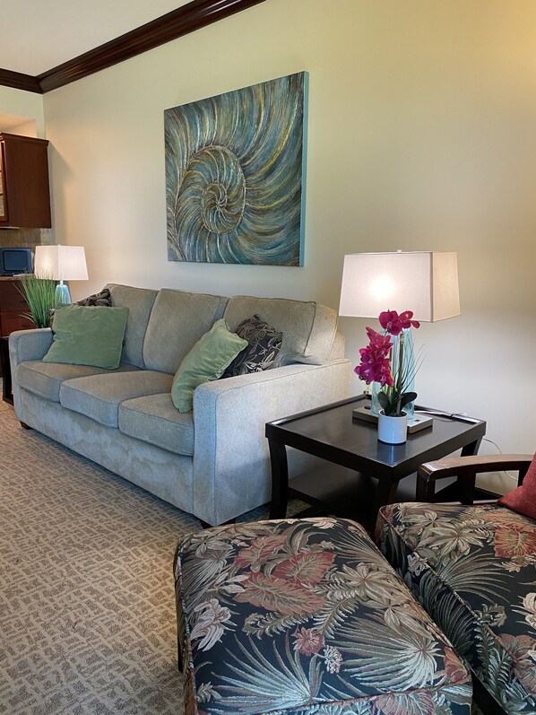 A living room with a sofa, two armchairs, a coffee table, a painting, a lamp, and a potted plant.