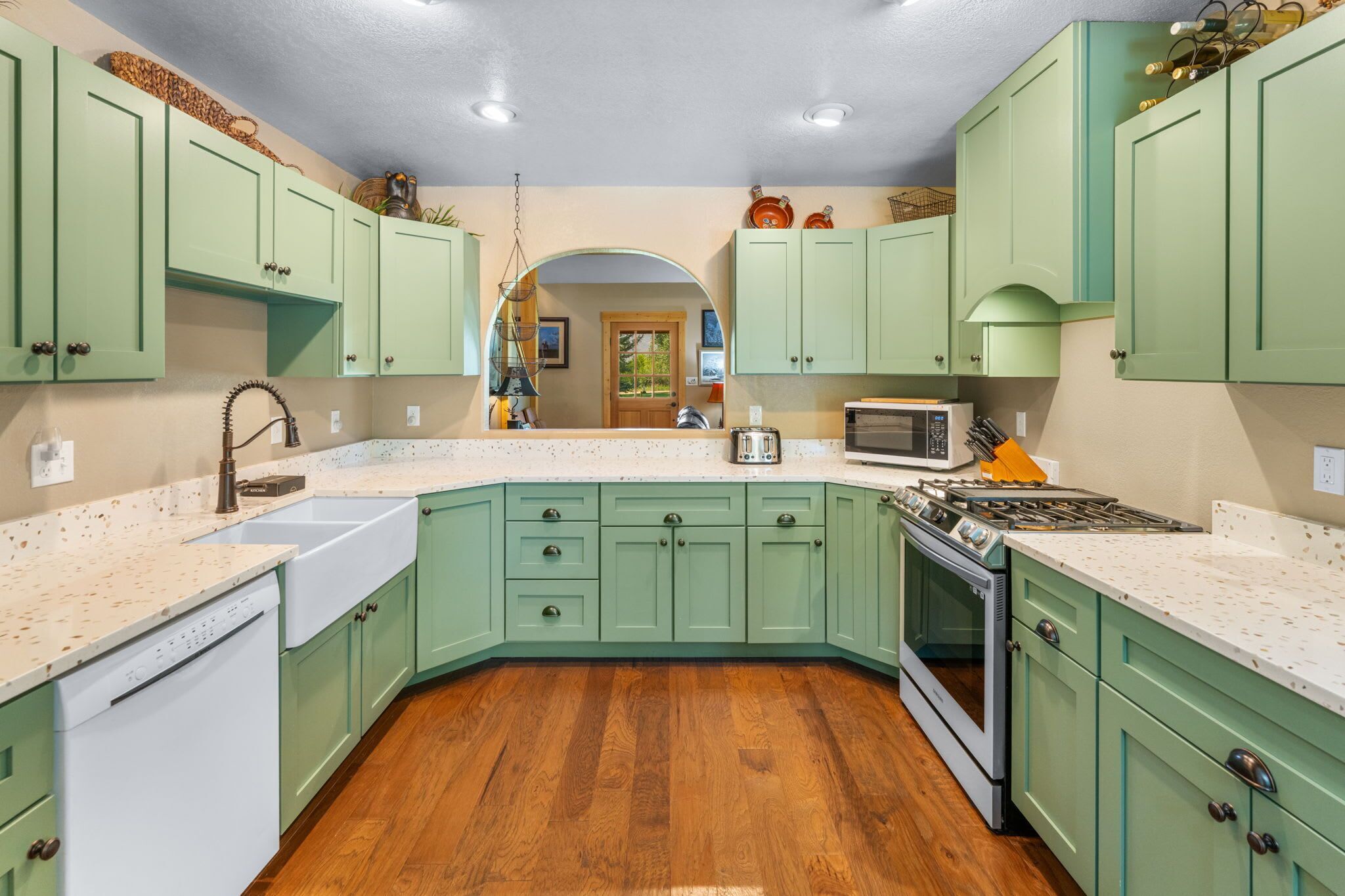 Una cocina con gabinetes verdes, encimera blanca, pileta, estufa y microondas.