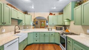 A kitchen with green cabinets, a white countertop, a sink, a stove, and a microwave.