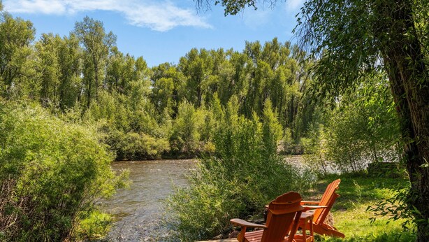 A river with surrounding greenery and two wooden Adirondack chairs facing the water.