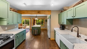 A kitchen with wooden flooring, green cabinets, a central island, and a view to a patio area.