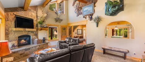 A cozy living room with a fireplace, leather sofa, mounted deer heads, and a television.