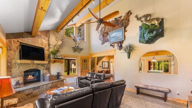 A cozy living room with a fireplace, leather sofa, mounted deer heads, and a television.
