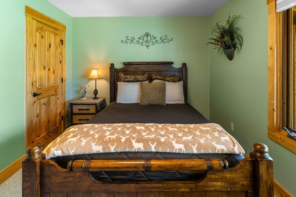 Un dormitorio con cama de madera, una mesita de noche con lámpara, un adorno en la pared y una planta en maceta.