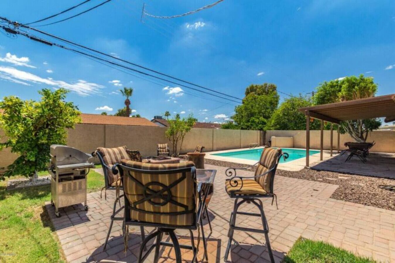 A backyard with a pool, outdoor furniture, and a barbecue grill.