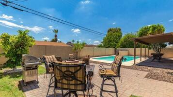 A backyard with a pool, outdoor furniture, and a barbecue grill.