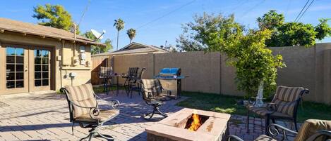 Un patio al aire libre con una chimenea, zona de estar y una parrilla.