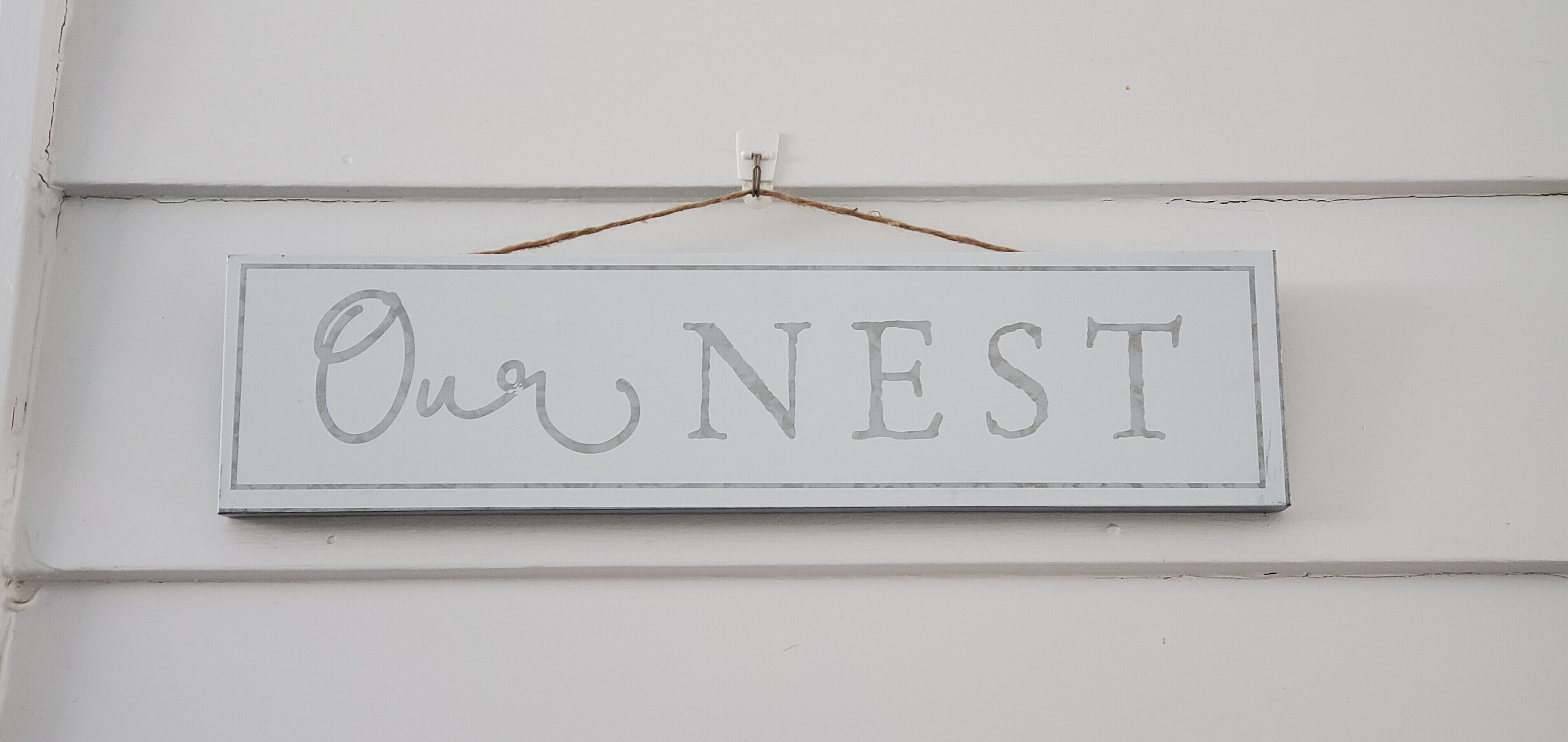 Un cartello con la scritta "Our NEST" appeso a una parete bianca.