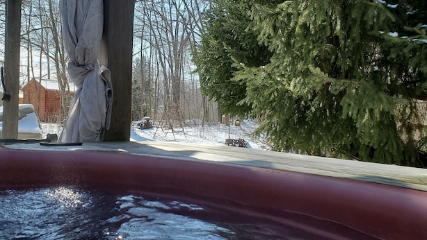 A hot tub with a view of a snowy yard and a large evergreen tree. - Your Home away from Home (Harbert)