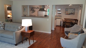A living room with a sofa, a lamp, and a coffee table. There is a kitchen area with a refrigerator, a sink, and a dining table with chairs. - Your Home away from Home (Harbert)