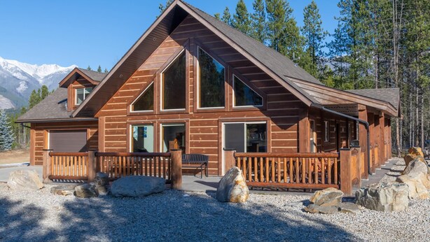 A log cabin with a large porch, multiple windows, and a view of snow-capped mountains. - Cranberry Cabin Rental (Valemount)