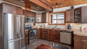 A modern kitchen with stainless steel appliances, wooden cabinets, and a window with blinds. - Cranberry Cabin Rental (Valemount)
