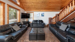 A spacious living room with leather sofas, a flat-screen TV, and a wooden staircase. - Cranberry Cabin Rental (Valemount)
