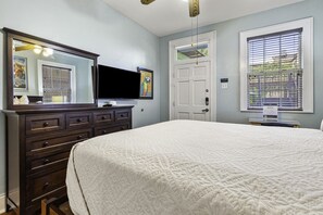 A bedroom with a large bed, a dresser, a television, and a door with a window.