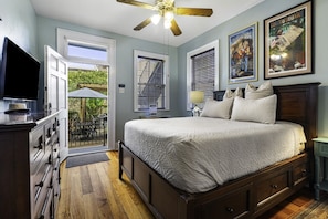 A bedroom with a bed, a television, a ceiling fan, and a window with blinds.