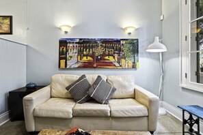 Ein Wohnzimmer mit einem beigefarbenen Sofa, gemusterten Kissen, einem Bild an der Wand und einer Stehlampe.