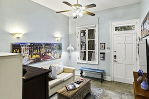 A living room with a sofa, a coffee table, a painting, a ceiling fan, and a window with a view.