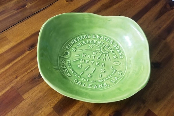 A green ceramic bowl with embossed text and symbols, placed on a wooden floor.