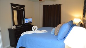 Une chambre à coucher avec un lit, un téléviseur posé sur une commode, un miroir, une lampe et une décoration en forme de cygne faite avec des serviettes.