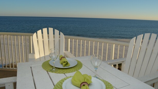 Une table dressée pour deux personnes, avec des chaises blanches, donnant sur une plage et l’océan en toile de fond.